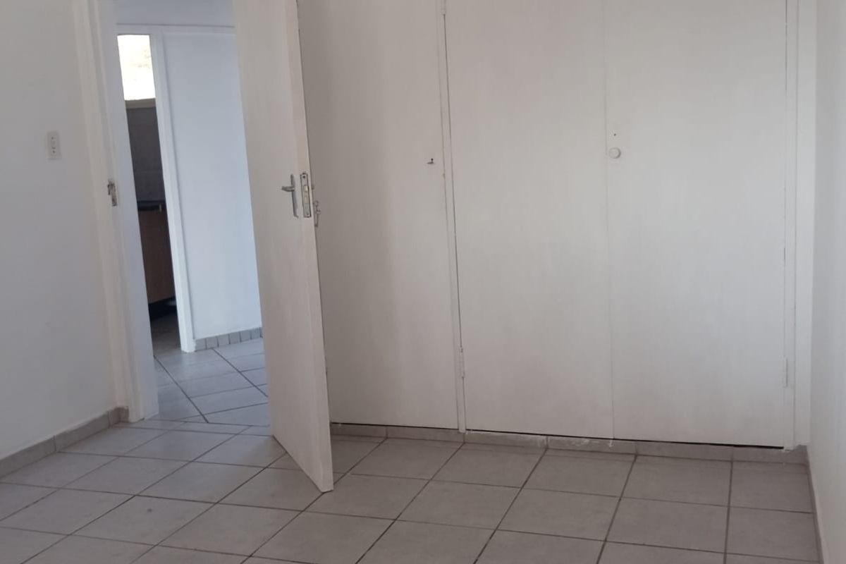 An empty bedroom featuring neutral tiled flooring and built-in cupboards, offering a clean and versatile space ready for personalization.