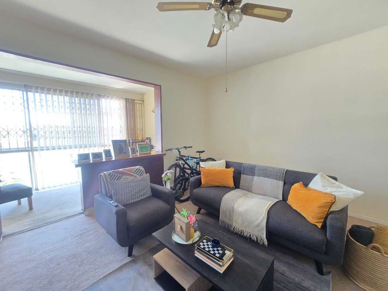 A living room featuring a ceiling fan and a large sliding glass door with a security gate leading to an adjacent space.