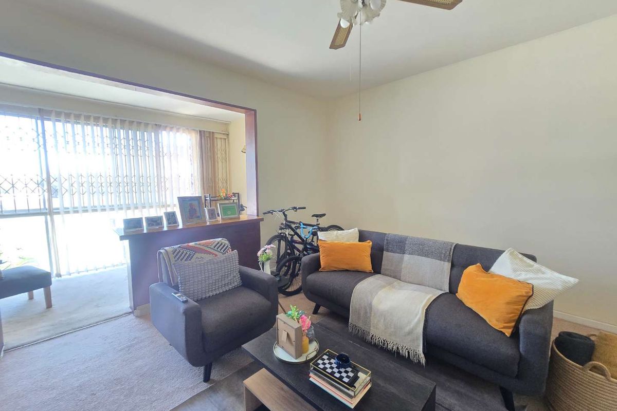 A living room featuring a ceiling fan and a large sliding glass door with a security gate leading to an adjacent space.