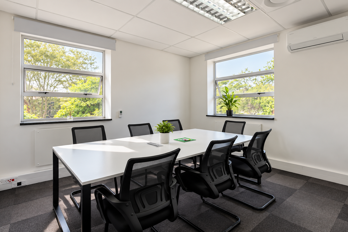 A bright, professional office meeting room featuring carpeted flooring, suspended ceiling with recessed lighting, split-system air conditioning, and large windows providing natural light.