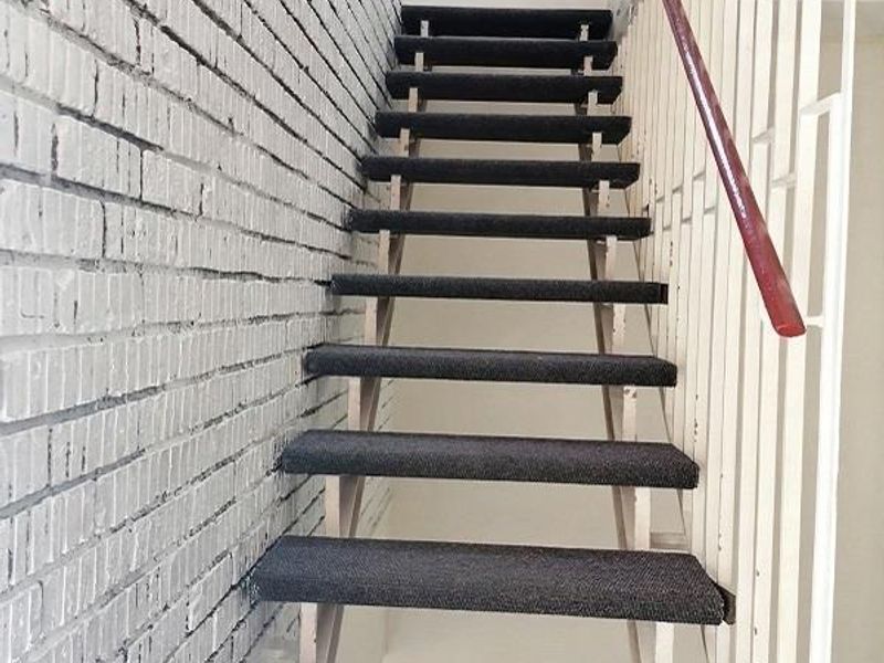 A staircase featuring a painted brick wall, metal balustrade, and wooden handrail, leading to an upper level.