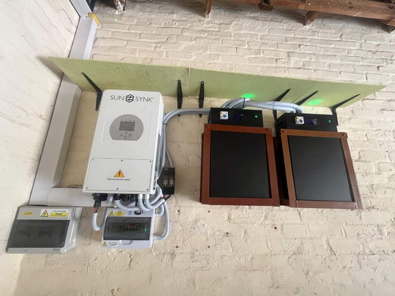 Wall-mounted solar inverter and dual lithium battery storage system installed on an exposed brick wall in a utility area.