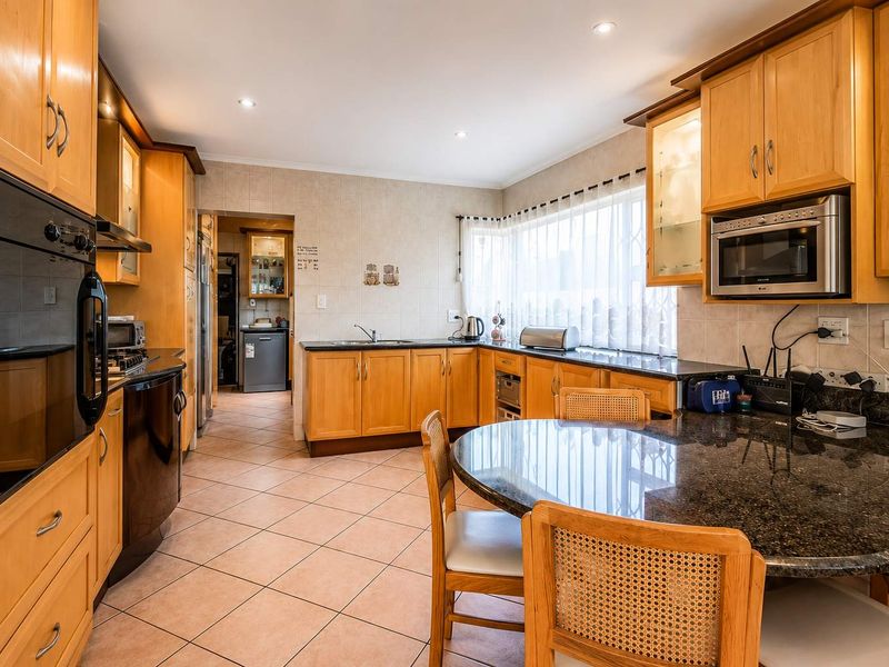 A functional kitchen featuring wooden cabinetry, granite countertops, tiled flooring, and built-in appliances, with an adjacent scullery area visible.