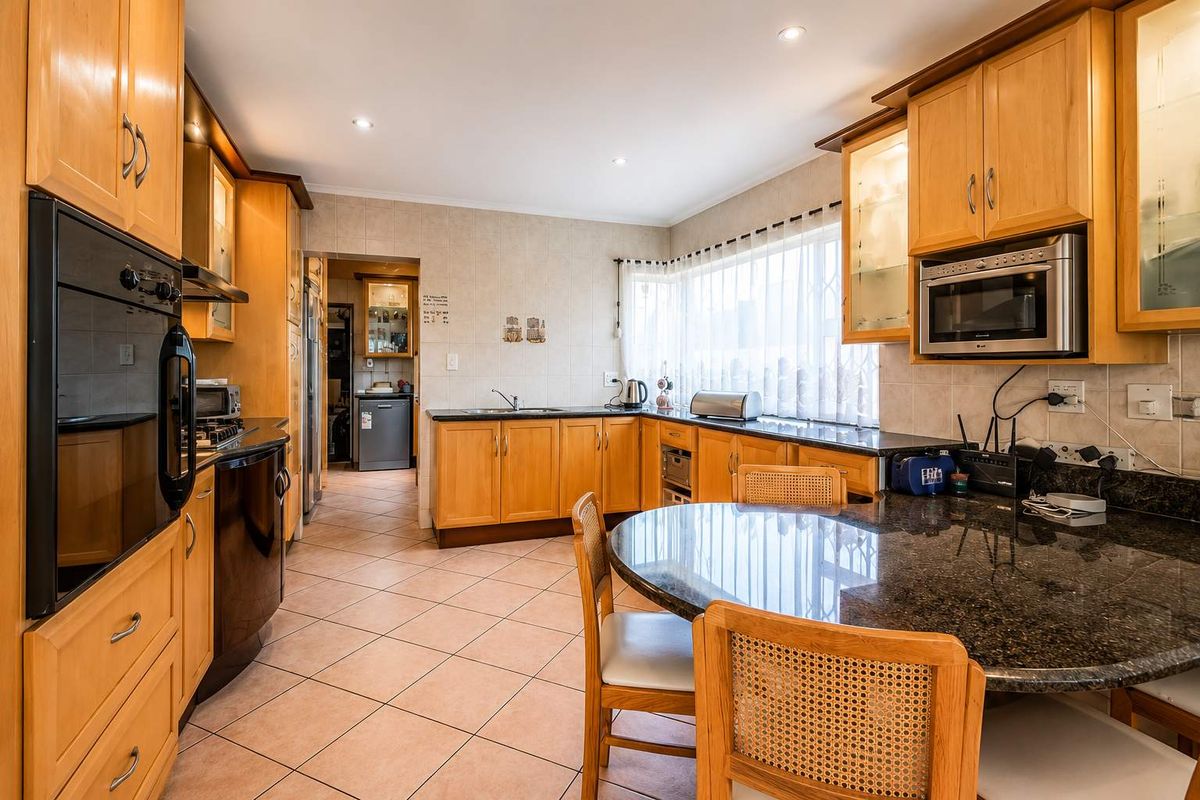 A functional kitchen featuring wooden cabinetry, granite countertops, tiled flooring, and built-in appliances, with an adjacent scullery area visible.