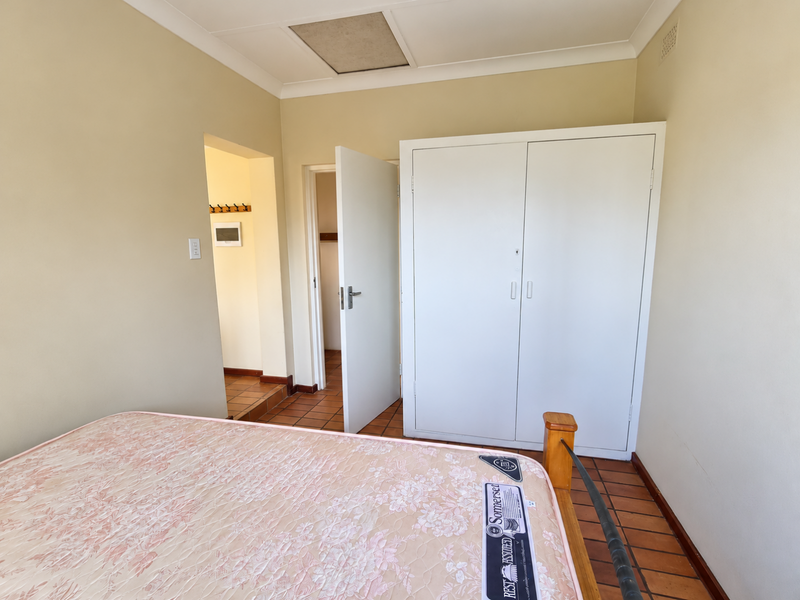A bedroom featuring tiled flooring, a built-in wardrobe, and a ceiling access hatch, leading into an adjacent hallway area.