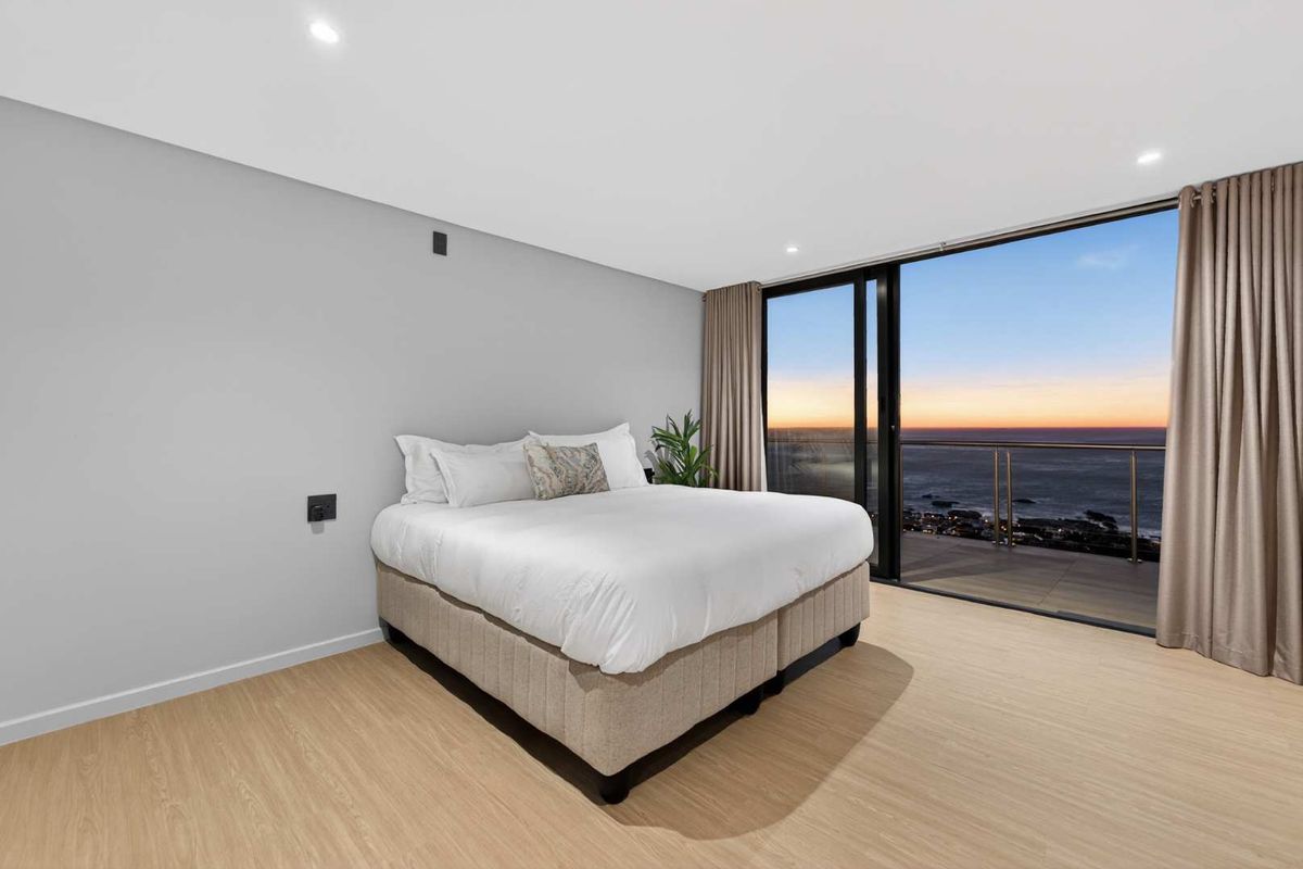 Modern bedroom featuring light laminate flooring, recessed lighting, and large sliding glass doors opening to a balcony with expansive ocean views.