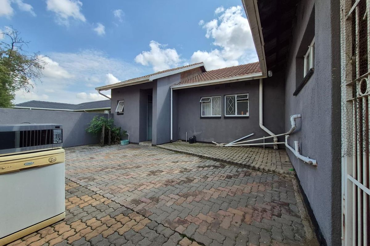 A rear exterior view of the property featuring a paved courtyard area, exposed exterior plumbing, and access to the main building structure.