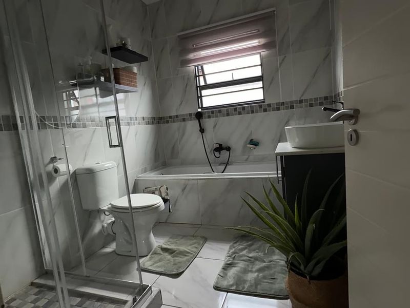 Modern bathroom featuring a glass shower enclosure, built-in bathtub, vanity with vessel sink, and marble-look wall tiling.