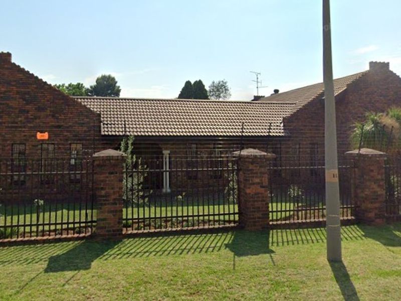 A well-maintained single-story face brick house featuring a tiled roof, secure perimeter wall with metal fencing, and a paved driveway.