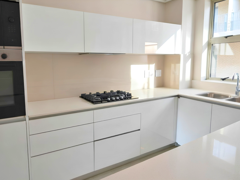 Modern kitchen featuring sleek white glossy cabinetry, stone countertops, integrated Bosch appliances, a gas hob, and a double bowl sink with a window view.