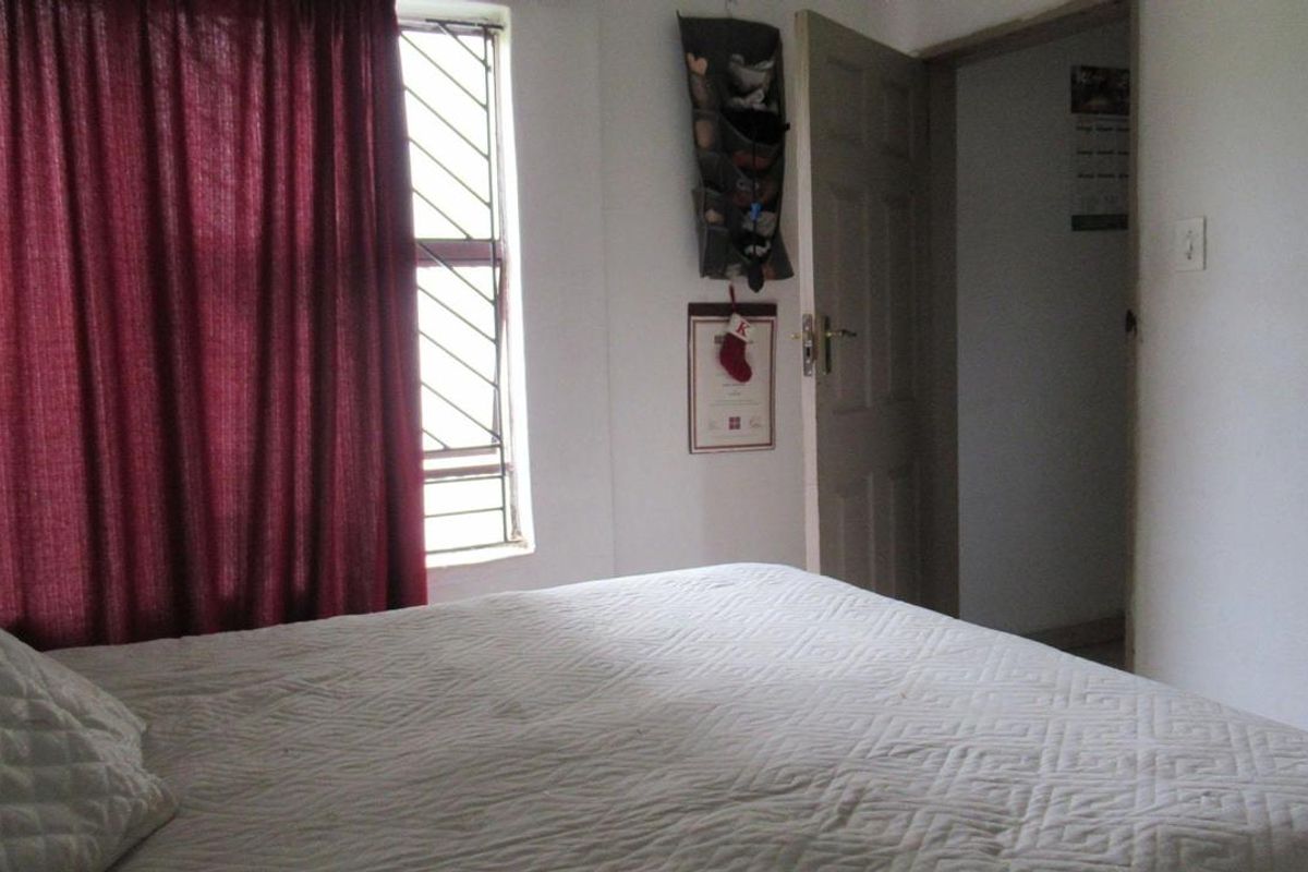 A functional bedroom featuring a window with security bars and a standard interior door, providing a simple and practical living space.