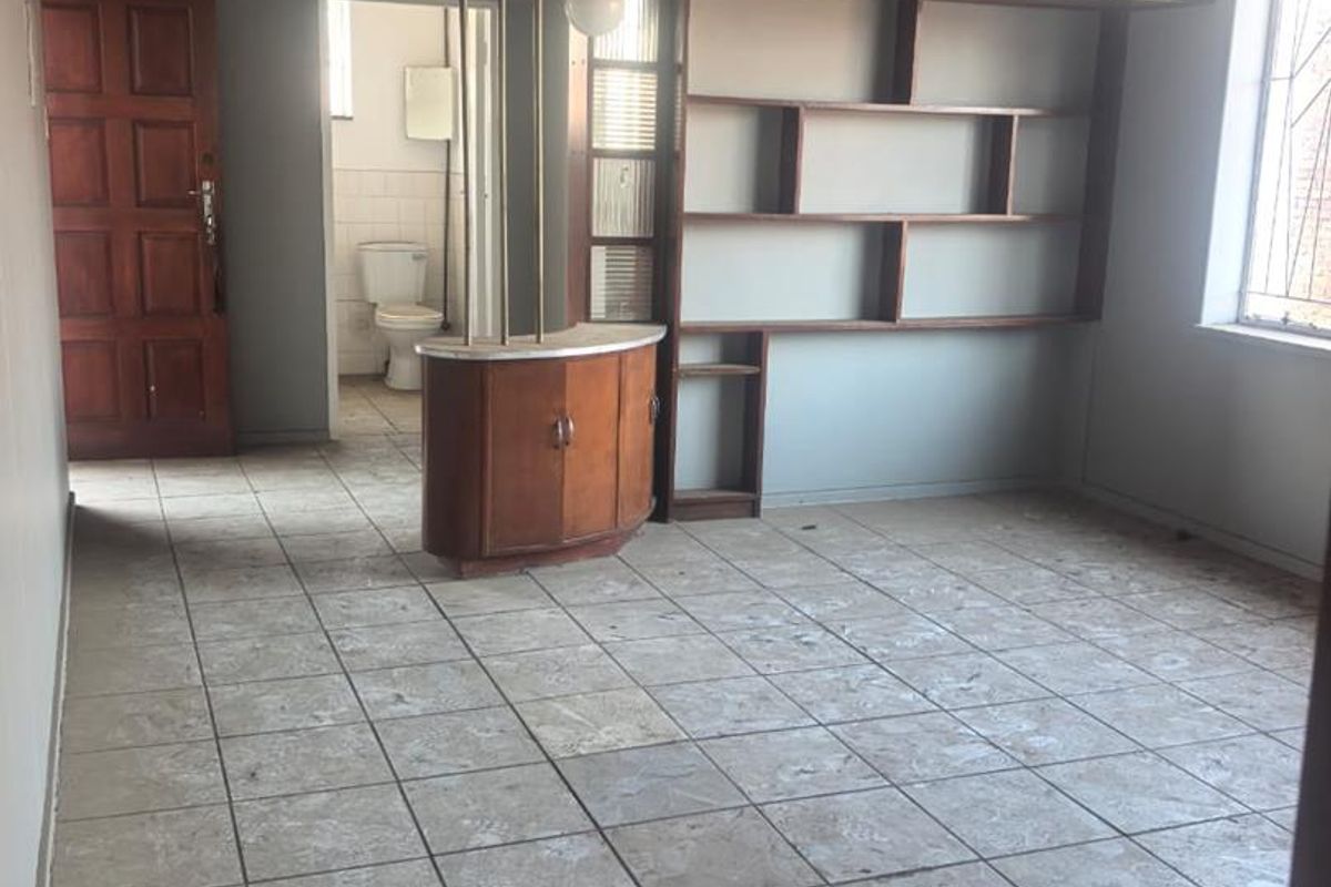 An empty living area featuring built-in shelving, overhead storage cabinetry, and tiled flooring, with an adjacent view into a bathroom.