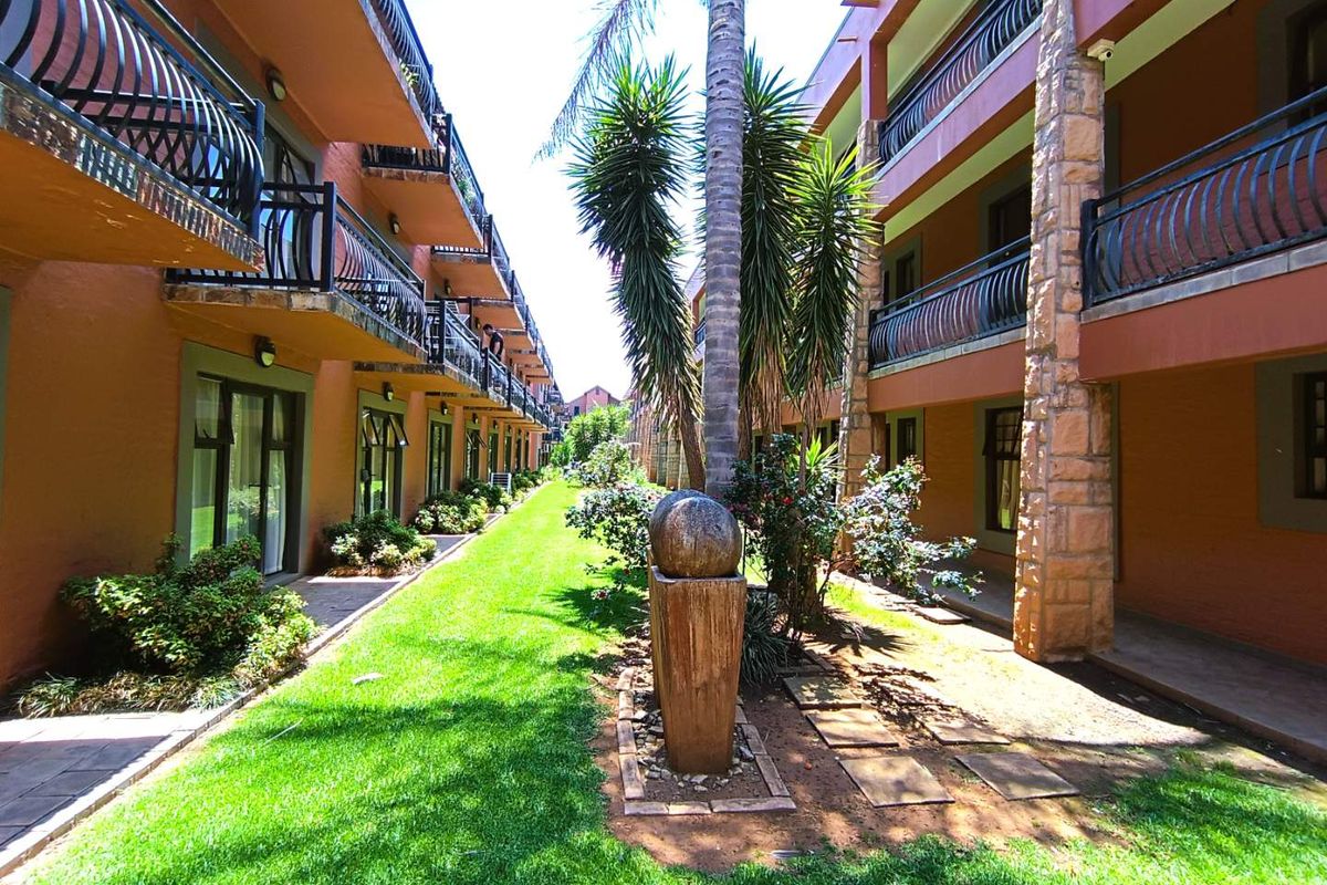 A landscaped courtyard area between apartment blocks featuring manicured lawns, established palm trees, stone pillars, and private balconies for each unit.