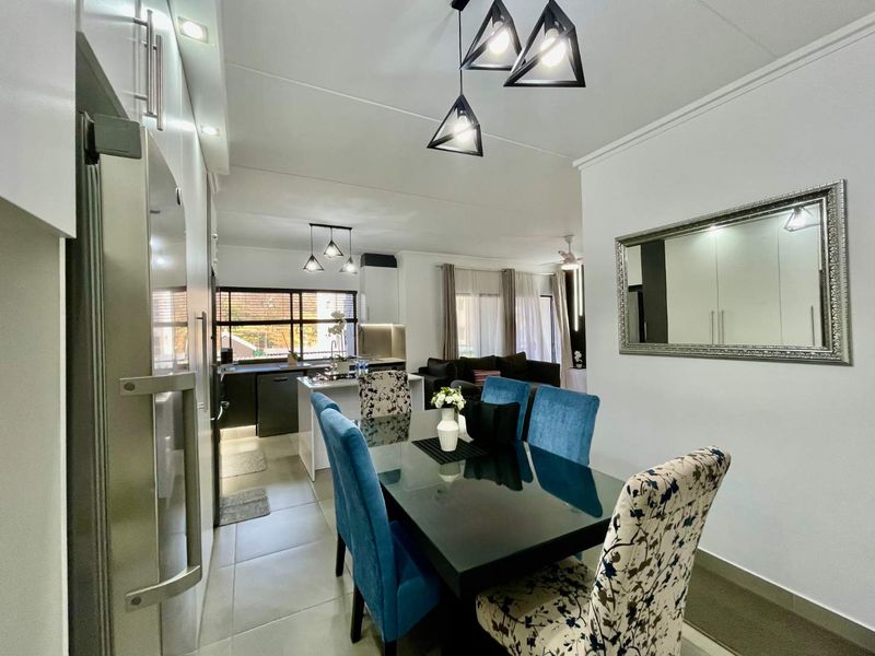 Modern open-plan living and dining area featuring a sleek kitchen with a central island, contemporary pendant lighting, and neutral tiled flooring throughout.