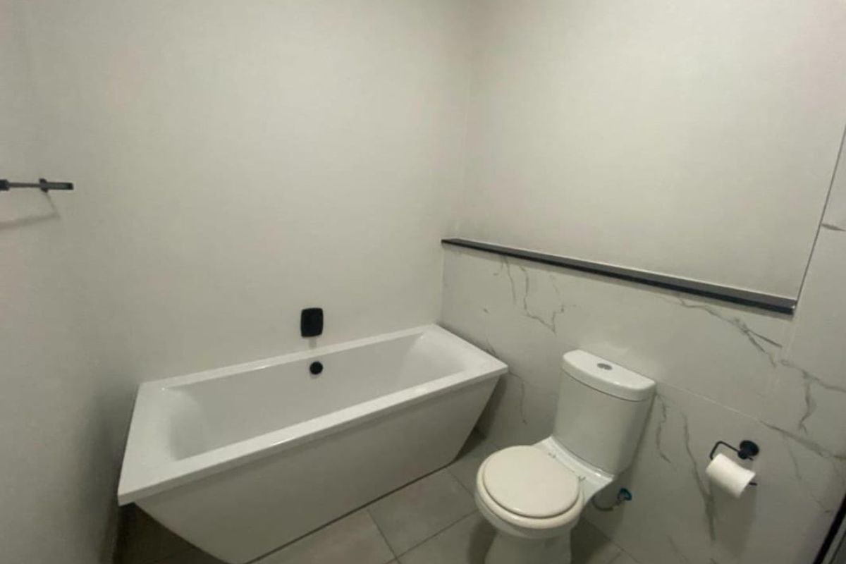 A modern bathroom featuring a white freestanding bathtub, a close-coupled toilet, and marble-effect wall tiling with black trim accents.