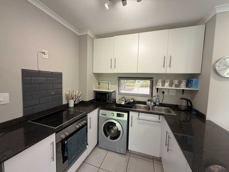 A functional kitchen featuring white cabinetry, dark granite countertops, a subway tile backsplash, and integrated appliances including an oven, hob, and washing machine.