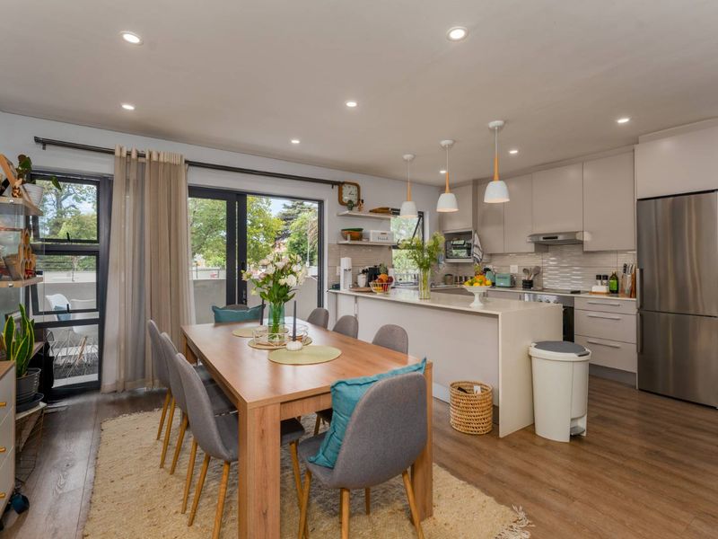 Modern open-plan living and dining area featuring a sleek kitchen with island, pendant lighting, and direct access to a balcony through sliding glass doors.