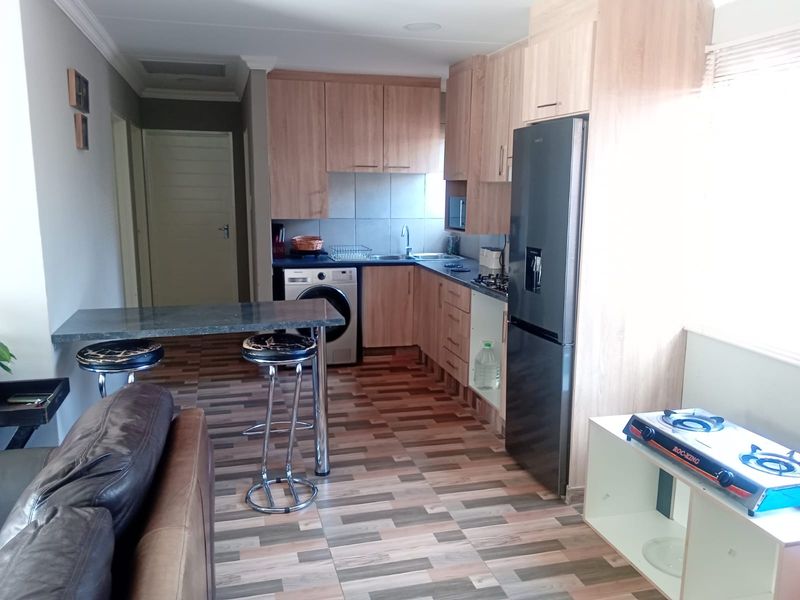 Open-plan kitchen and living area featuring wood-look cabinetry, tiled flooring, and a breakfast bar counter.