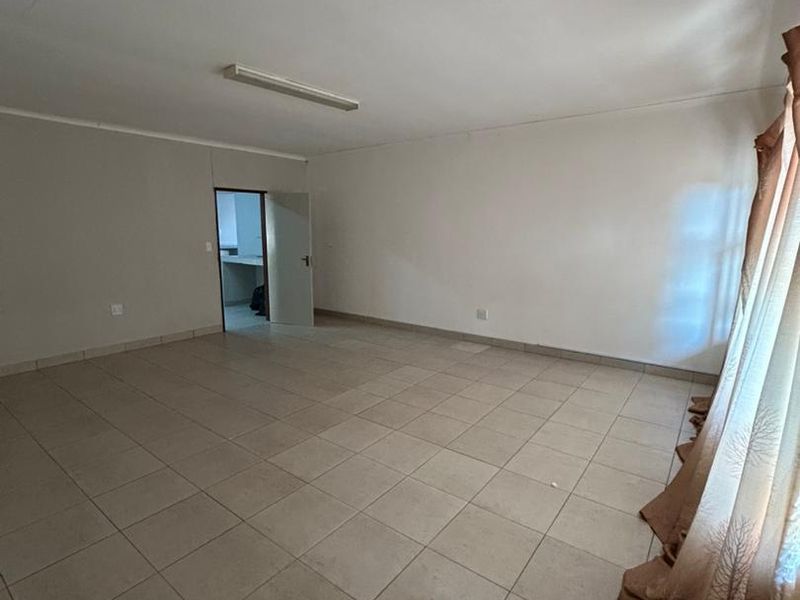 A spacious, empty living area featuring neutral tiled flooring and a simple ceiling light fixture, offering a blank canvas for interior design.