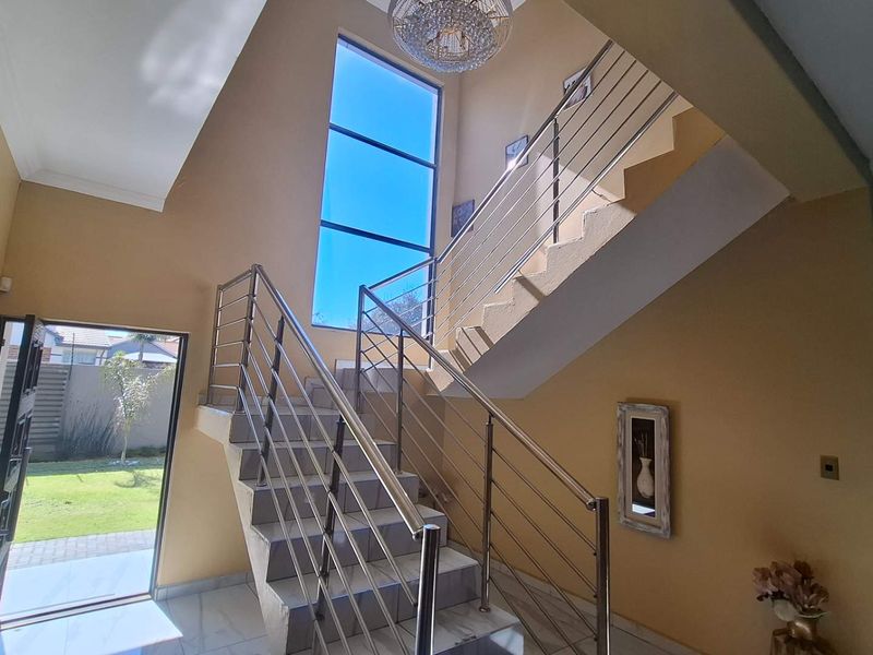 Spacious double-volume entrance hall featuring a modern staircase with stainless steel balustrades, large feature window, and elegant tiled flooring.