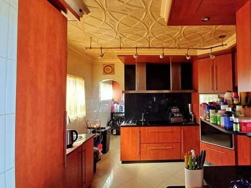 A kitchen featuring wood-toned cabinetry, a decorative ceiling, integrated appliances, and tiled flooring, offering a functional layout with ample storage space.