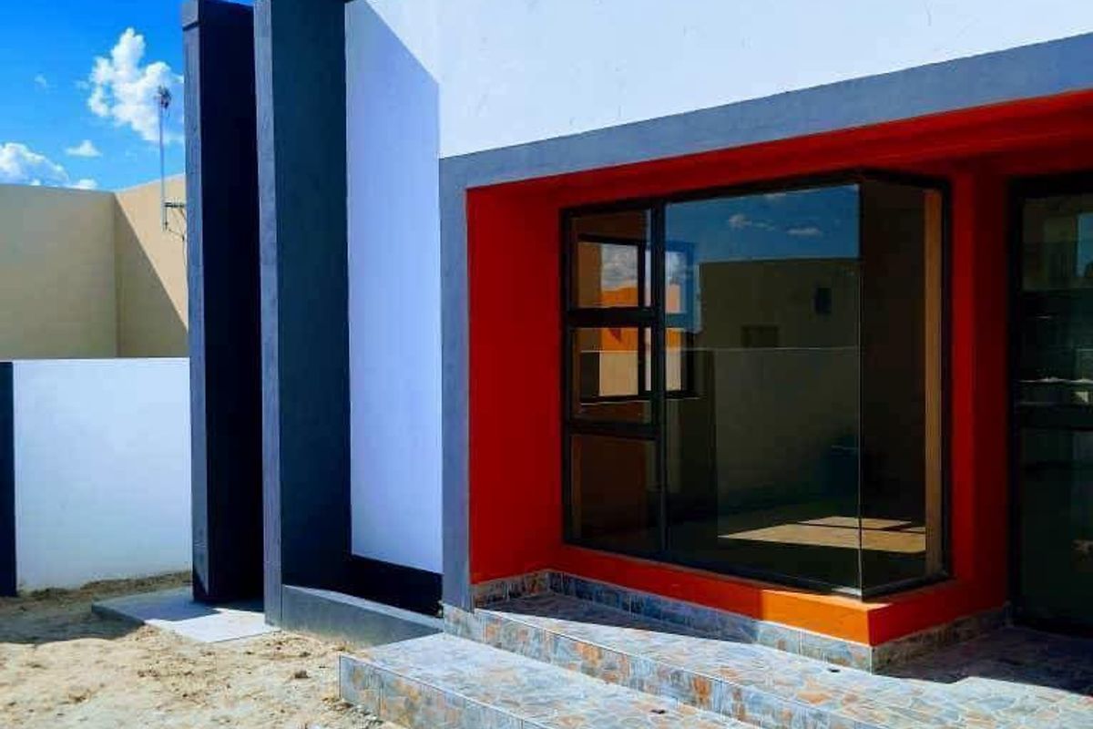 Modern front facade featuring a bold red accent wall, large bay window, and tiled entrance steps, currently awaiting final landscaping completion.