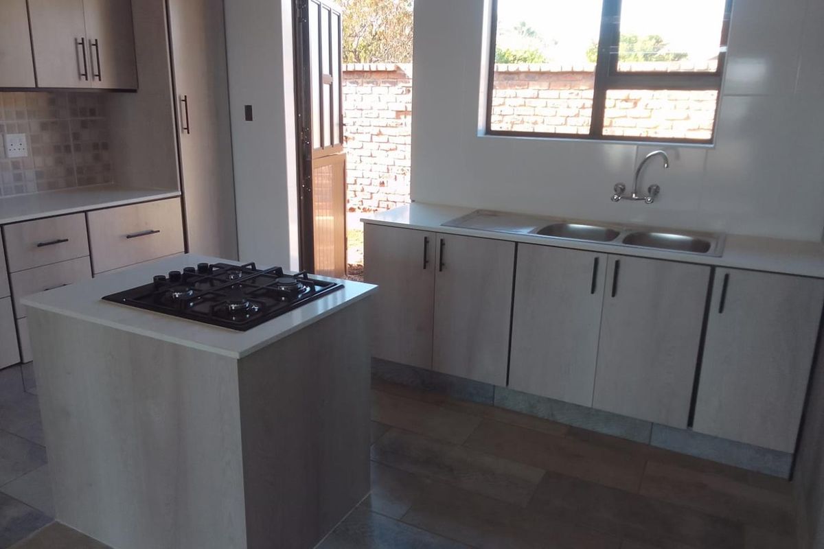Modern kitchen featuring light wood-finish cabinetry, a central island with a built-in gas hob, double sink, and direct access to an outdoor area.