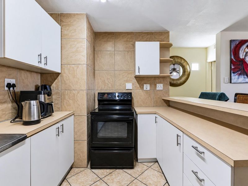 A functional kitchen featuring white cabinetry, laminate countertops, a tiled backsplash, and a breakfast bar overlooking the adjacent living area.