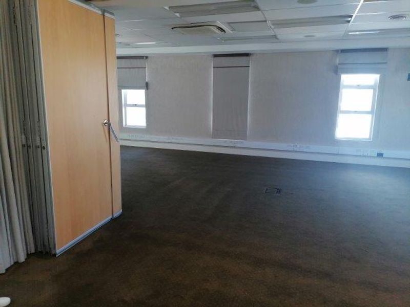 An open-plan office space featuring a folding partition wall, suspended ceiling with integrated air conditioning, and carpeted flooring.