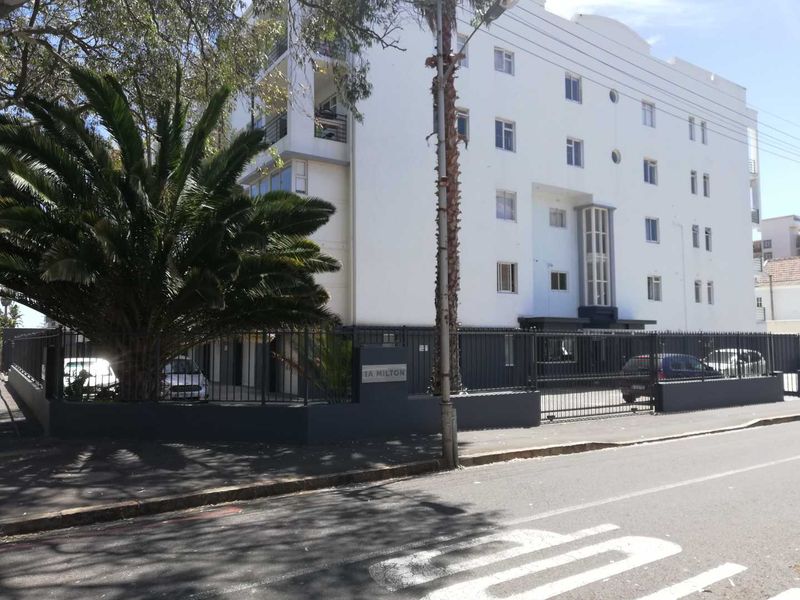 Street view of the apartment building facade featuring a secure perimeter fence, gated entrance, and multi-level balconies.