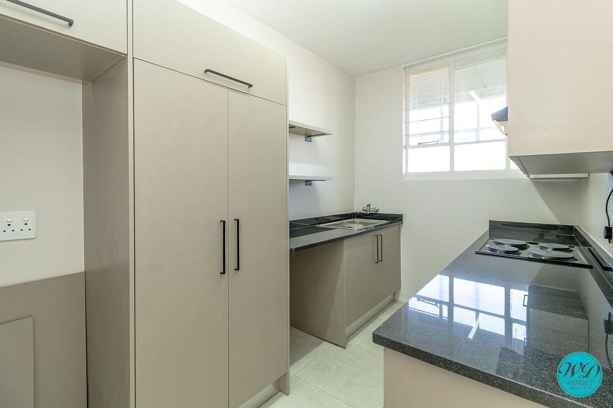 Modern kitchen featuring sleek built-in cabinetry, dark granite countertops, an integrated electric hob, and a stainless steel sink with tiled flooring.