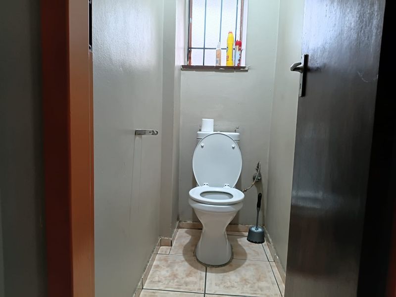 A compact, functional bathroom featuring a standard toilet, tiled flooring, and a small window with security bars.