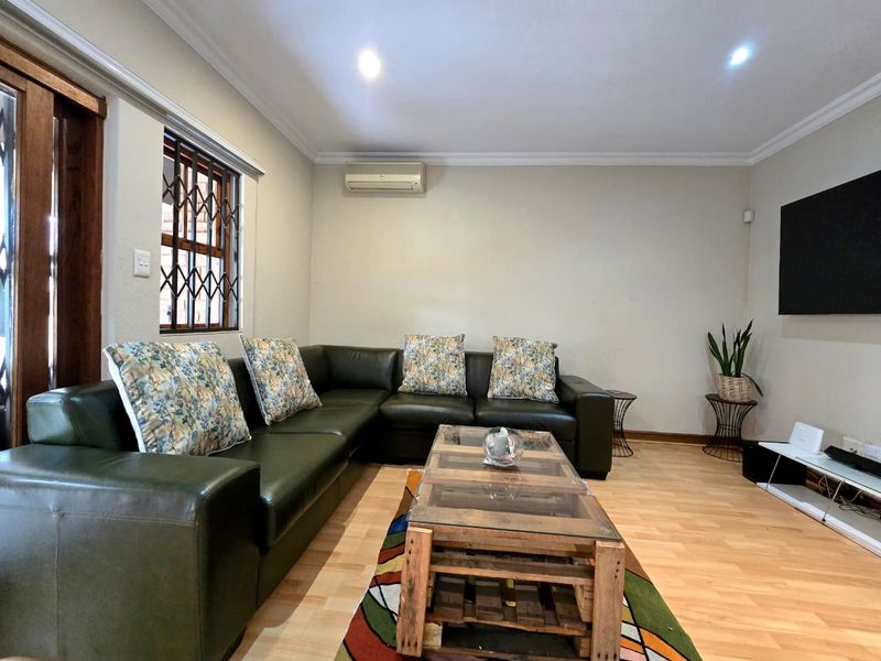 A well-maintained living room featuring laminate flooring, recessed downlighting, and a wall-mounted air conditioning unit.