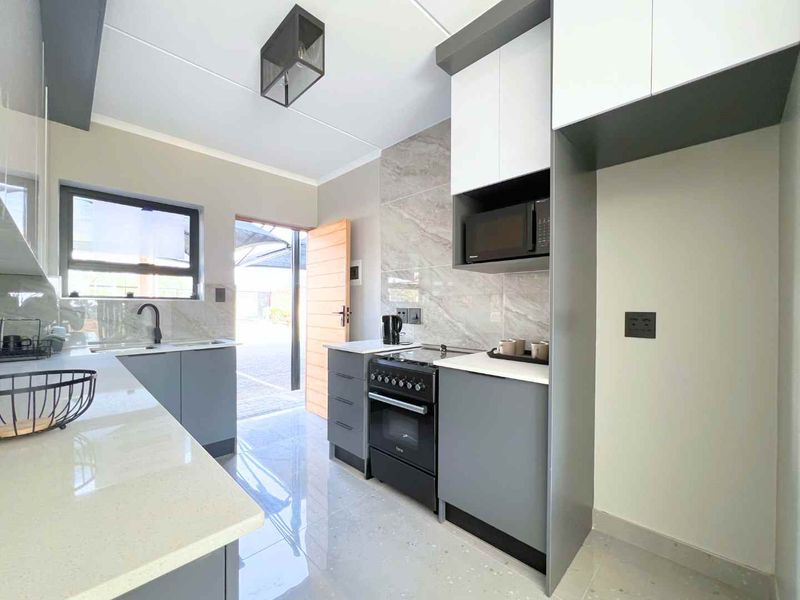 Modern kitchen featuring sleek grey cabinetry, quartz countertops, stone-look splashback, built-in microwave, and a freestanding stove, with direct access to an outdoor area.