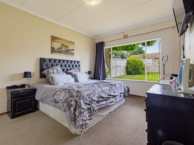 A spacious bedroom featuring large windows with garden views, neutral wall tones, and carpeted flooring, offering a comfortable and well-lit living space.