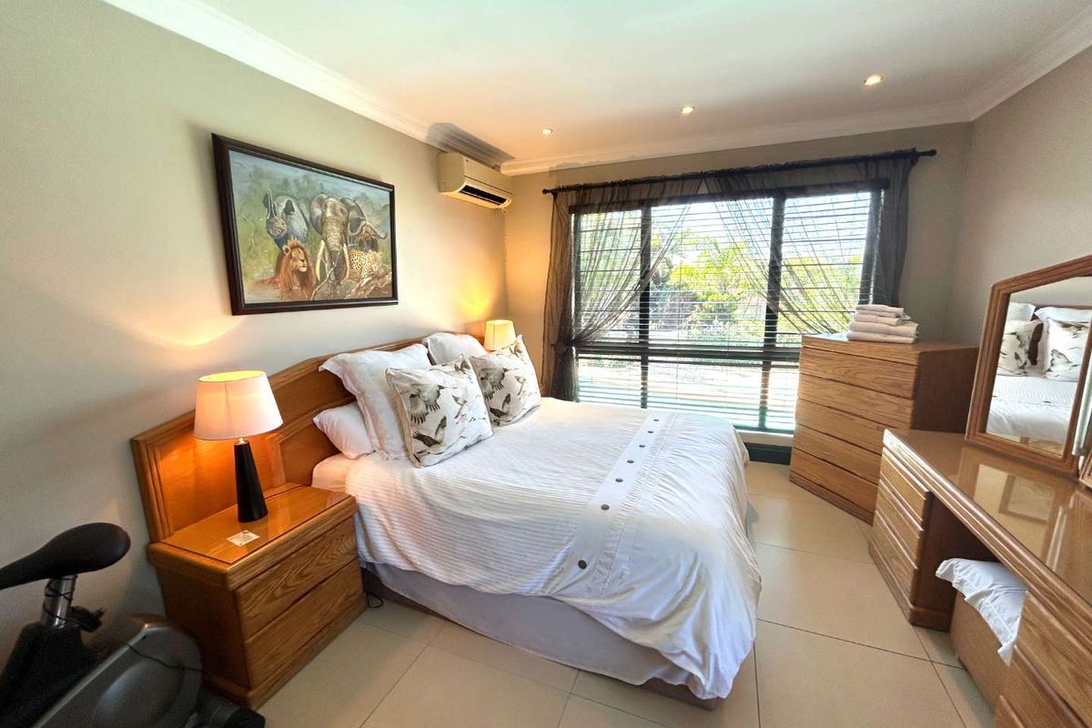 A well-lit bedroom featuring tiled flooring, a wall-mounted air conditioning unit, and large windows with blinds.