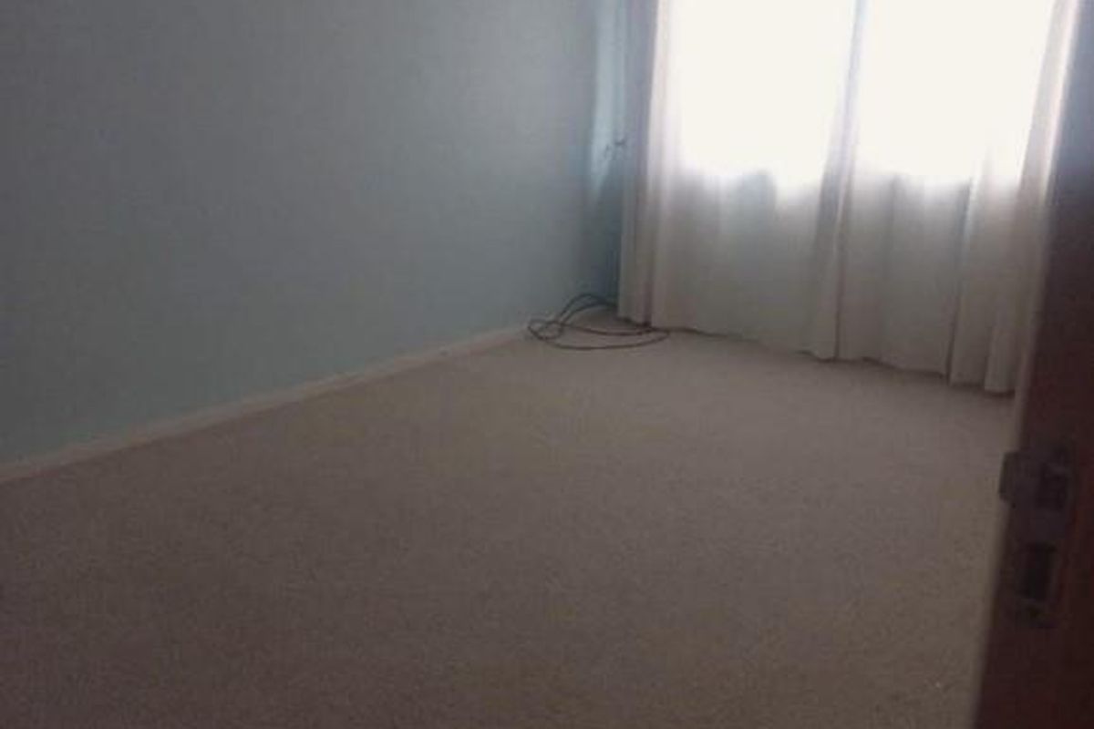 A vacant bedroom featuring neutral carpeting, light blue walls, and a wall-mounted air conditioning unit.