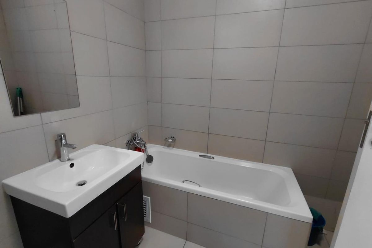 A functional bathroom featuring a modern vanity with basin, a bathtub with shower mixer, and neutral wall tiling.