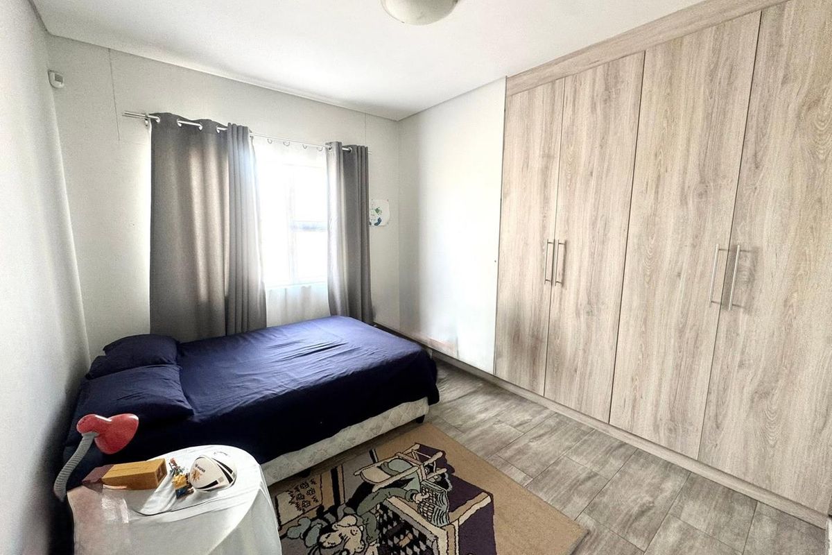 A well-maintained bedroom featuring light wood-grain built-in cupboards, modern laminate flooring, and a neutral color palette.