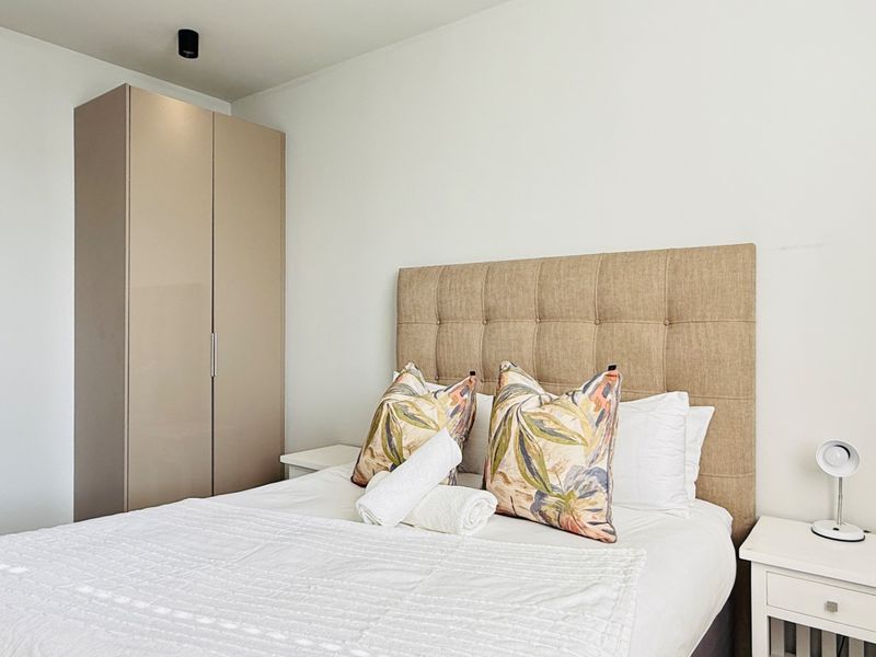 A well-maintained bedroom featuring a neutral color palette, a built-in wardrobe, and a modern upholstered headboard.