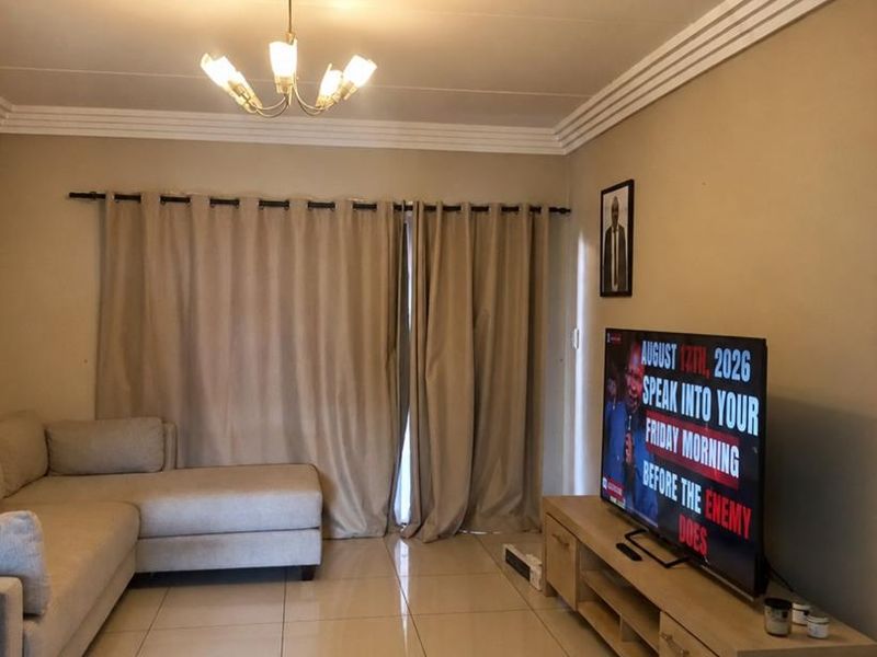 A well-maintained living room featuring neutral tiled flooring, decorative ceiling cornices, and a central light fixture, providing a clean and functional living space.