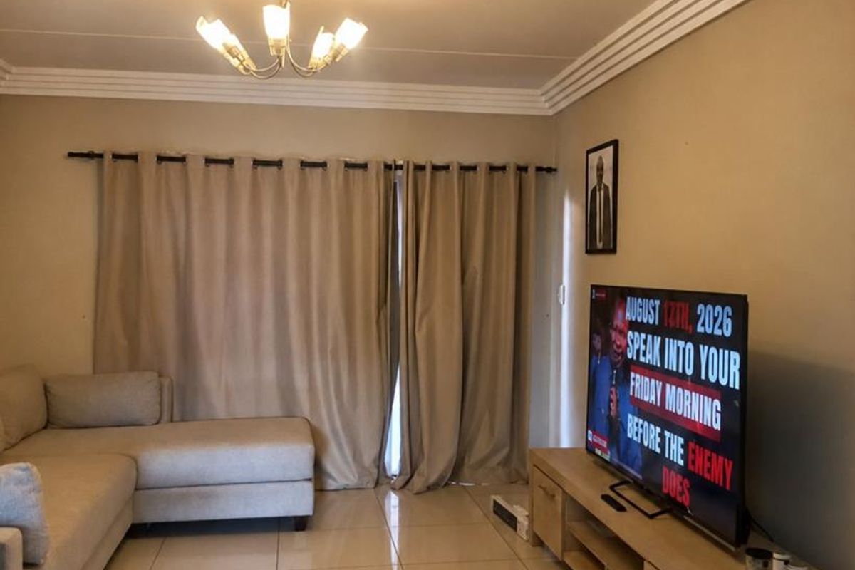A well-maintained living room featuring neutral tiled flooring, decorative ceiling cornices, and a central light fixture, providing a clean and functional living space.
