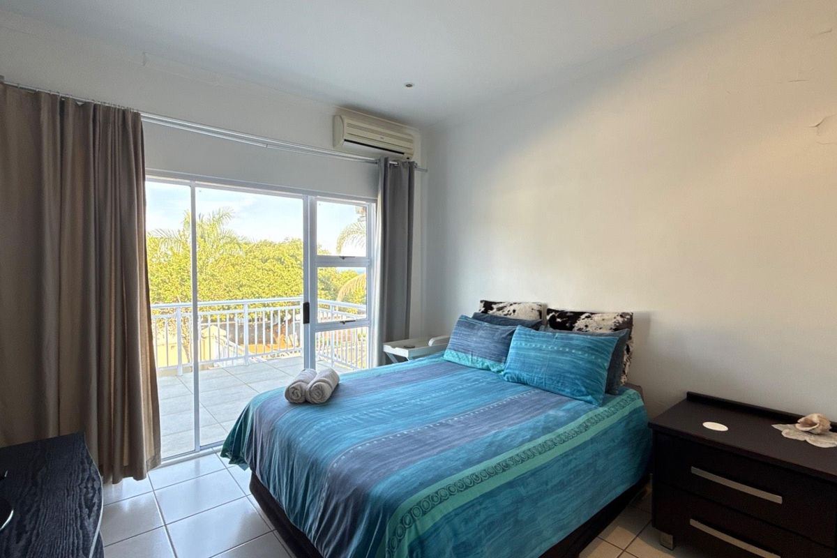 A bedroom featuring tiled flooring, a wall-mounted air conditioning unit, and sliding glass doors leading to an outdoor balcony.