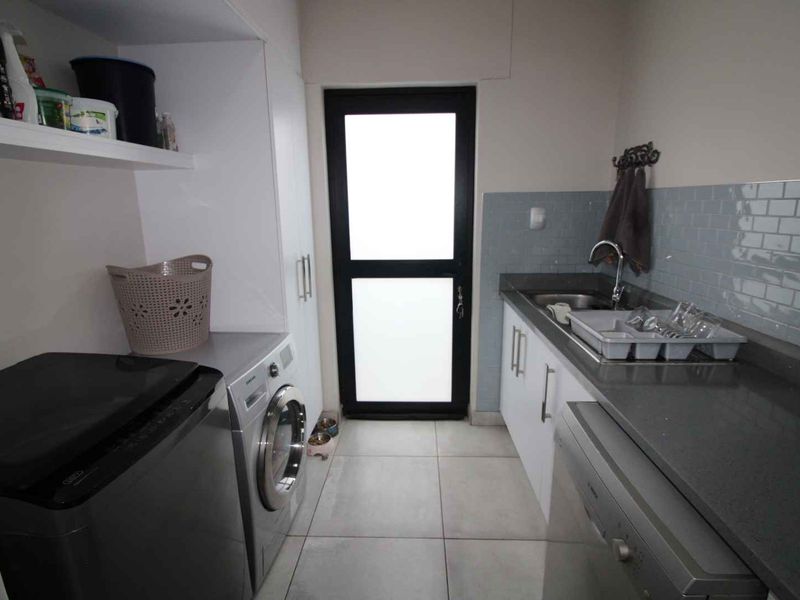 A functional laundry room featuring built-in cabinetry, stone countertops, a subway tile backsplash, and direct access to the exterior.