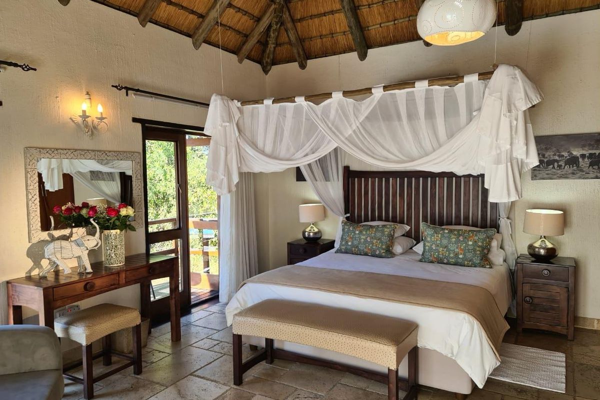 A well-maintained bedroom featuring a traditional thatched roof, stone flooring, and direct access to an outdoor balcony area.