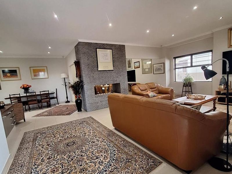 Spacious open-plan living and dining area featuring a central stone-clad fireplace, neutral tiled flooring, and recessed downlighting throughout.