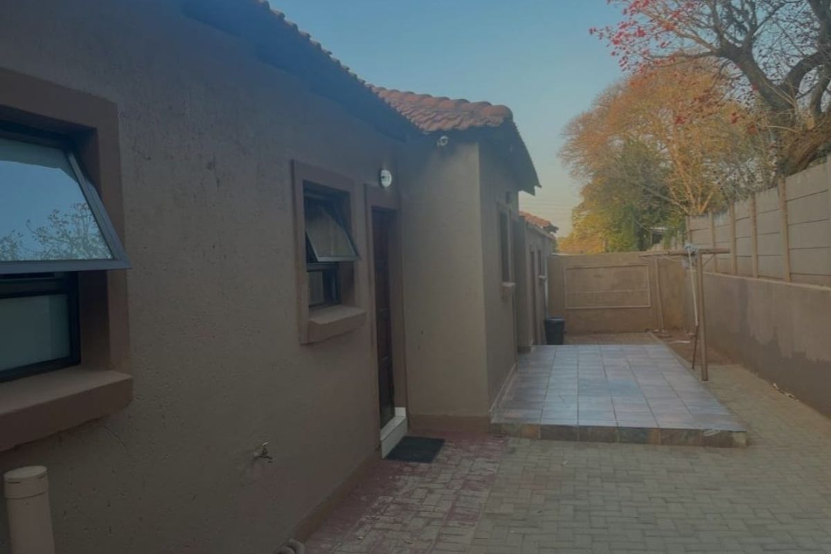 A view of the rear exterior of the townhouse, featuring a paved patio area, tiled walkway, and perimeter walling.