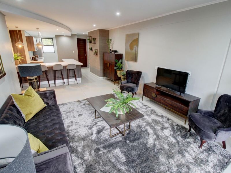 A modern open-plan living area featuring a sleek kitchen with a breakfast bar, recessed lighting, and polished tiled flooring throughout.