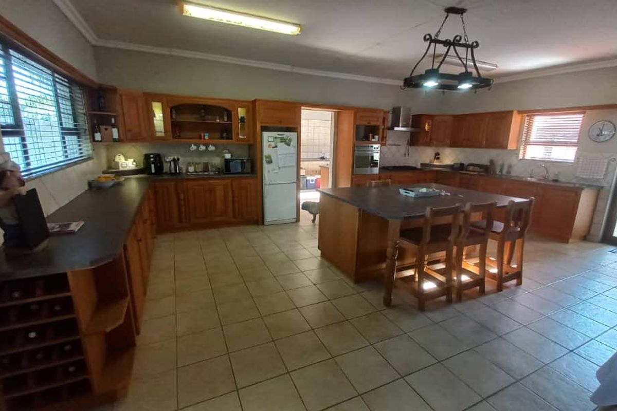 Spacious kitchen featuring extensive wooden cabinetry, a large central island, built-in oven, extractor fan, and tiled flooring with direct access to the outdoor area.