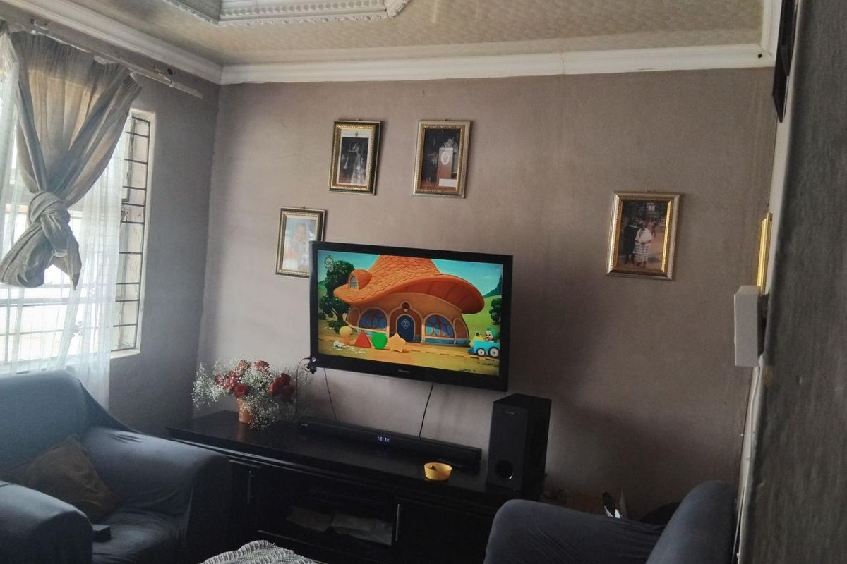 A living room featuring a wall-mounted television, decorative ceiling molding, and a window with security bars.